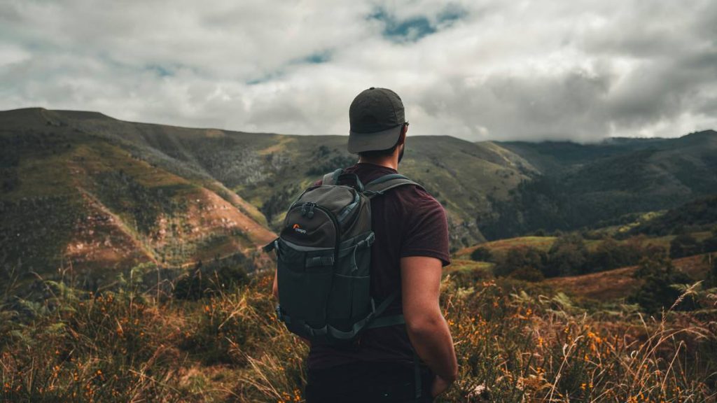 Man in a hat with backpack looks in the distance in the beautiful nature.