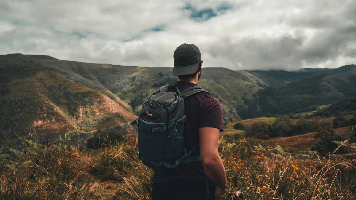 Man in a hat with backpack looks in the distance in the beautiful nature.