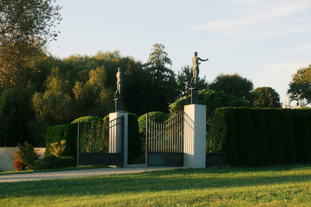Ornate gates with statues lead to a tree-lined estate.