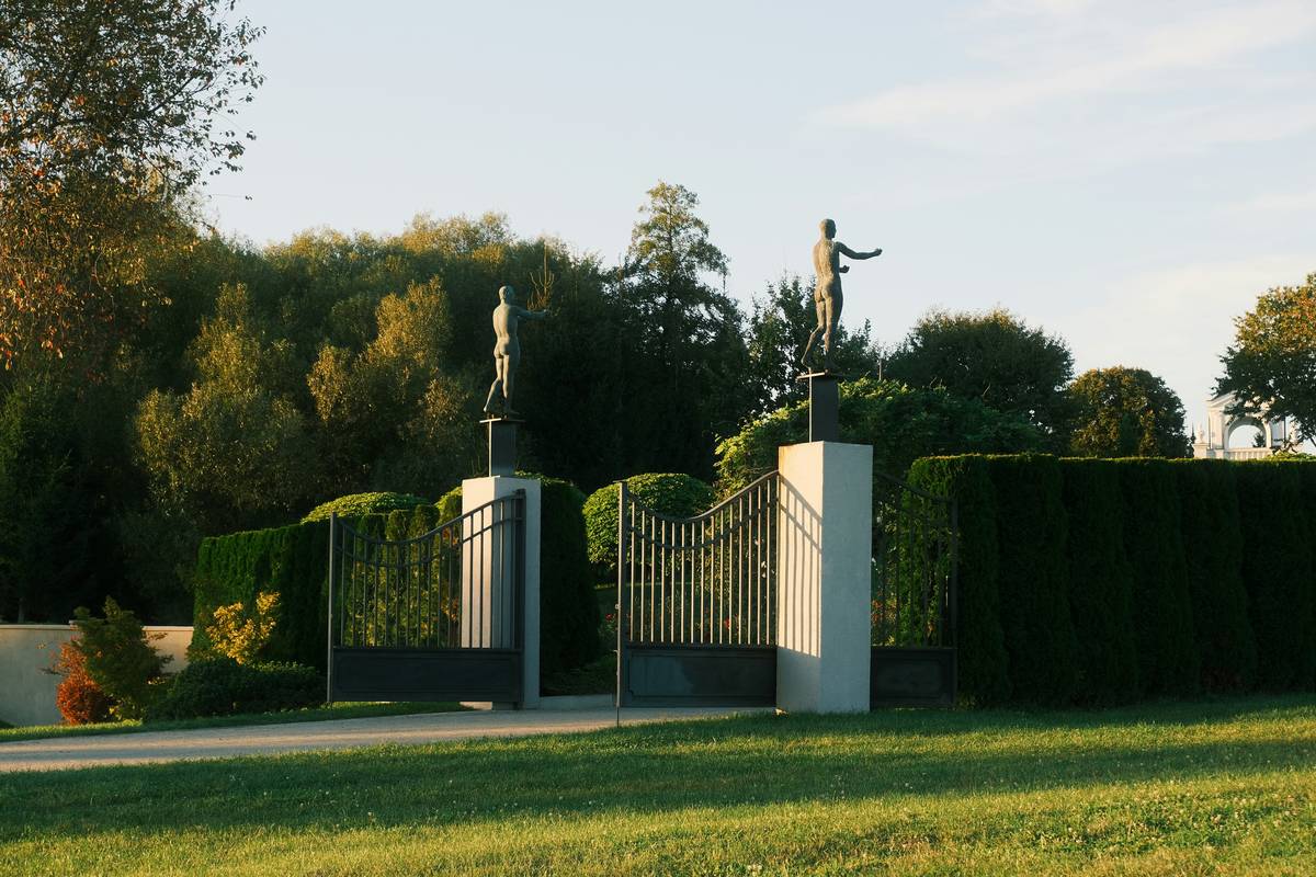 Ornate gates with statues lead to a tree-lined estate.